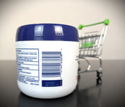 A white plastic jar with a dark blue lid, showing the back label and barcode, set on a dark surface with a miniature shopping cart in the blurred background.
