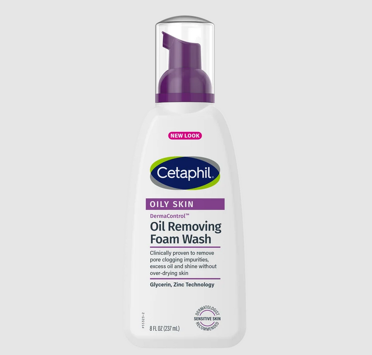 A bottle of Cetaphil Oily Skin Oil Removing Foam Wash on a light gray background. The bottle is white with a purple pump and features the Cetaphil logo in green and blue.